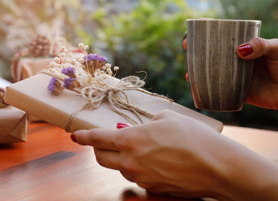 En hånd som holder i en bok som er innpakket i brunt gavepapir og hyssing og pyntet med små fiolette og hvite blomster. 