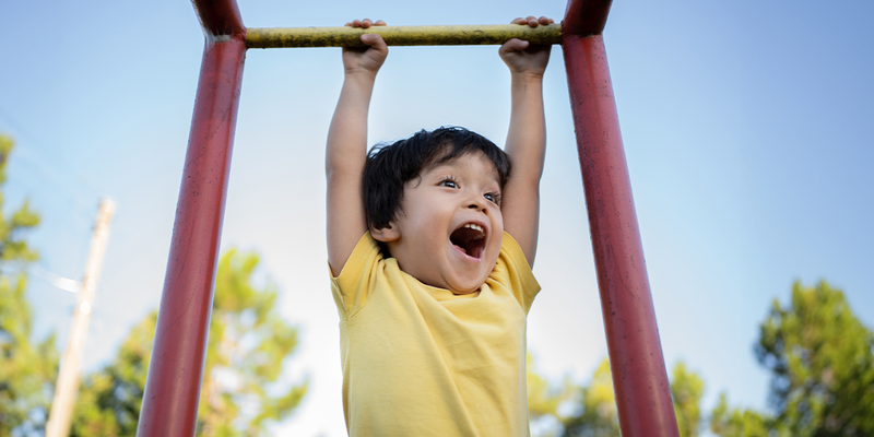 En ung gutt smiler mens han henger i en klatrestativ på en lekeplass, som fanger de siste sommerdagene før fotoknudsen sine tips til en morsom og organisert skolestart.