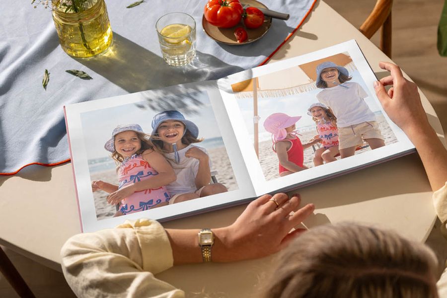 En åpen fotobok på et kjøkkenbord viser bilder av unge jenter som har det gøy på stranden, som illustrerer fotoknudsen sitt tips om å se tilbake på sommerminner med en personlig fotobok.