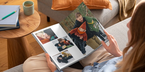 En kvinne ser i en fotobok med layflat-binding fra fotoknudsen med familriebilder i snøen, perfekt når du skal lage din egen fotobok eller et fotoalbum.