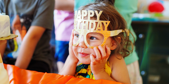 En liten jente med morsomme Happy Birthday-briller, ser etter en personlig bursdagsgave eller bursdagsgave tips fra fotoknudsen.