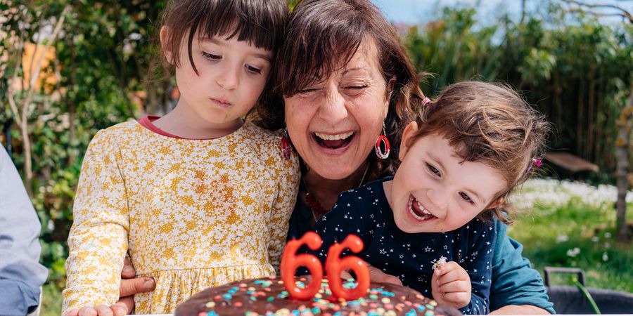En kvinne smiler ved siden av bursdagskaken sin med lys som viser '66', flankert av en liten jente og en liten gutt, som introduserer fotoknudsen sin ultimate bursdagsgaveguide.