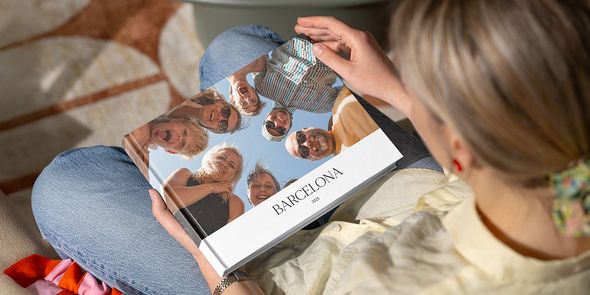 En kvinne ser på en fotobok med titelen 'Barcelona', med et bilde av mange smilende familieansikter som ser ned i kameraet, som illustrerer fotoknudsen sin guide til å lage en gruppefotobok fra ferien.