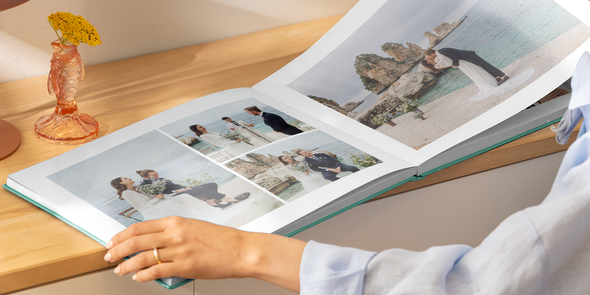 Kvinnehender som holder en oppslått bryllupsfotobok med en dobbeltside med ulike strandbilder av en brud og en brudgom, som illustrerer fotoknudsen sine ideer til titler på bryllupsfotoboken.