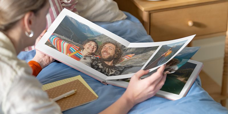 fotoknudsen fotobok-inspirasjon: En kvinne ser på en åpen fotobok med et dobbeltsidig oppslag av et par i et fjellandskap.