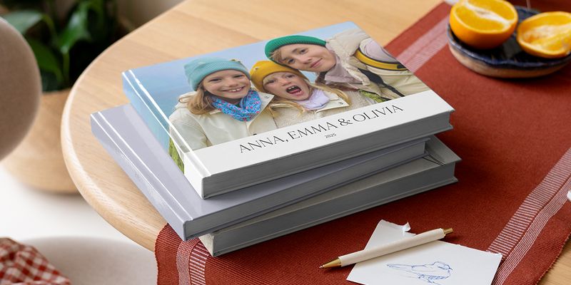 Et utvalg av fotobøker fra fotoknudsen på et bord med en penn, som viser søsken på omslaget som inspirasjon til norske sitater og hva man skal skrive i et fotoalbum.