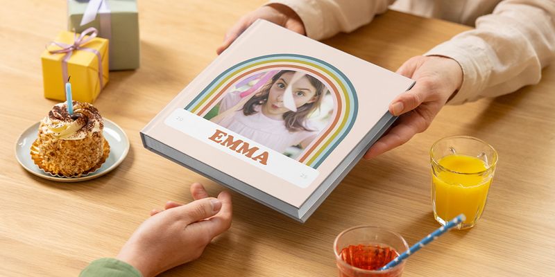 En fotobok til bursdag for Emma sendes over et bord med kake og gave, som viser en personlig bursdagsgave og et fotoalbum fra fotoknudsen.