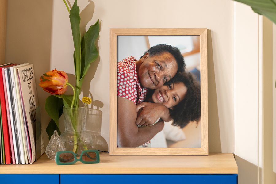 Et innrammet bilde av en bestemor og barnebarn som klemmer står på et bord ved siden av bøker, et magasin og en dekorativ vase, som inspirasjon til rammetrender og rimelige måter å løfte veggdekor på.