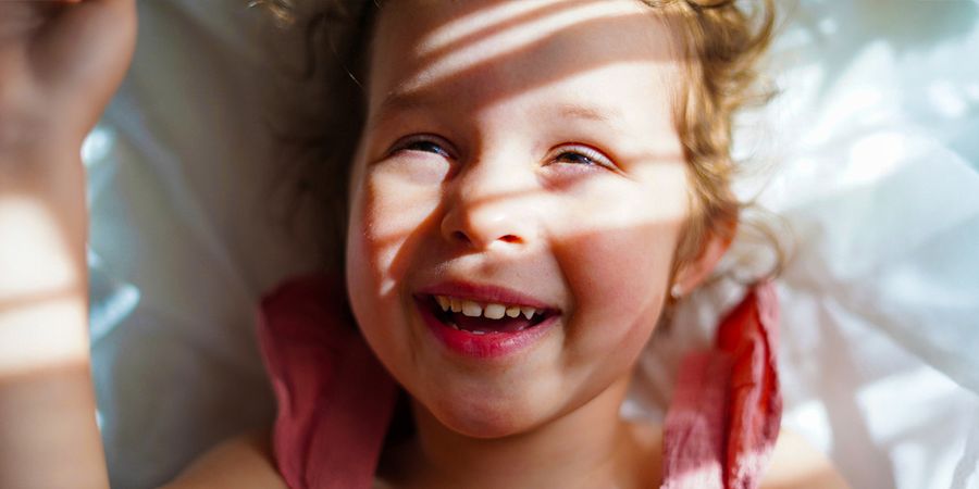 En smilende liten jente med sollys og myke skygger i ansiktet, som inspirasjon til fotoknudsen tips om hvordan ta gode bilder i sterkt sollys.