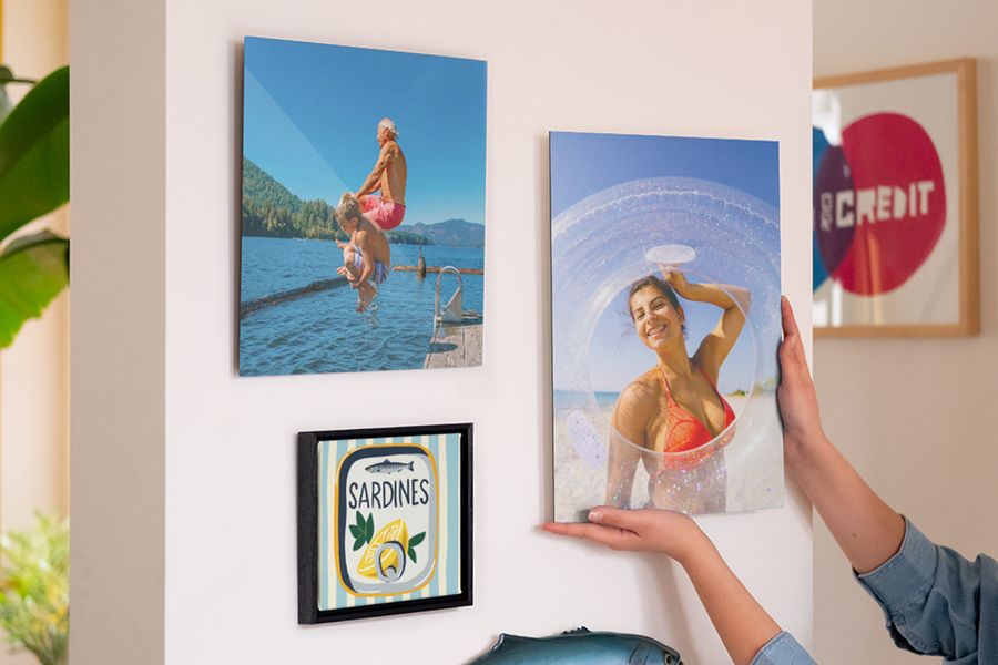 En bildevegg med personlig fotoknudsen veggdekor viser en smilende kvinne på stranden, en mann og en gutt som hopper i sjøen, og en illustrasjon av en sardineboks, som inspirasjon til å innrede sommerlig hjemme.
