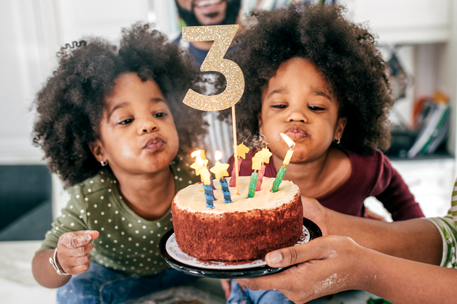 To tvillingjenter som skal blåse ut lysene på kaken til 3-årsdagen sin, som viser personlige bursdagsgaver og bursdagsgave tips fra fotoknudsen.