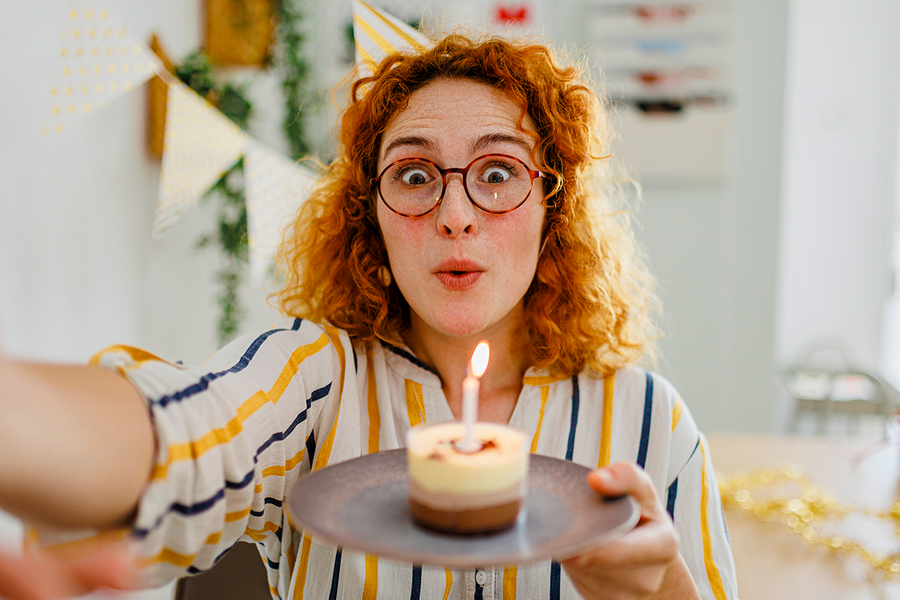 En kvinne med rødt krøllete hår holder en cupcake med et lys, som inspirasjon til bursdagshilsener til en kollega og bursdagskort fra fotoknudsen.
