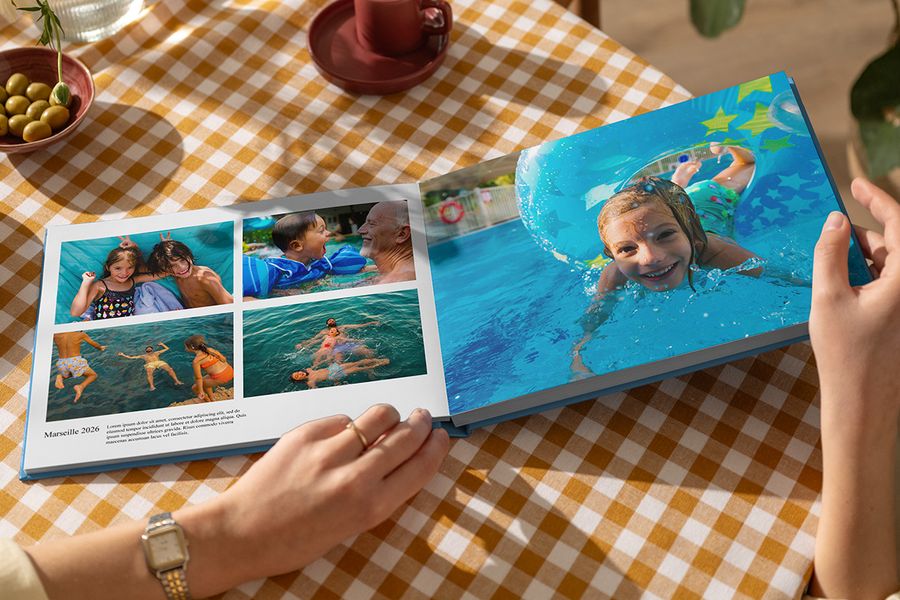 En åpen fotoknudsen feriealbum viser sommerlige familiebilder av lek i vannet, med ett stort oppslag og en annen side med tittelen Marseille 2026, bildetekst og beskrivelse, som illustrerer hvordan tekst gjør en personlig fotobok reise levende.