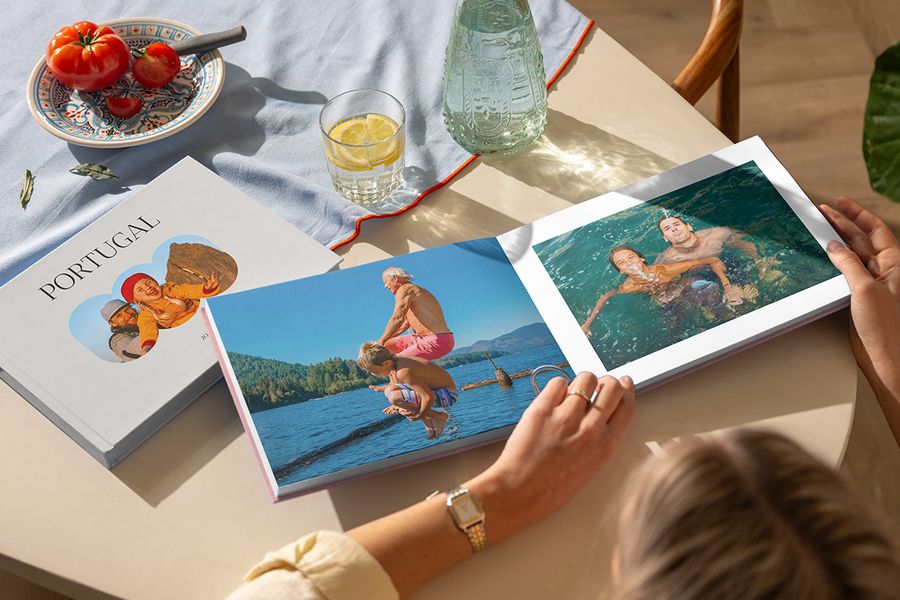 To ulike fotoknudsen reisealbum vises, mens en kvinne blar i en åpen fotobok reise med familiebilder fra sjøen, ved siden av en lukket Portugal-bok, som illustrerer et personlig feriealbum fullt av reiseminner.
