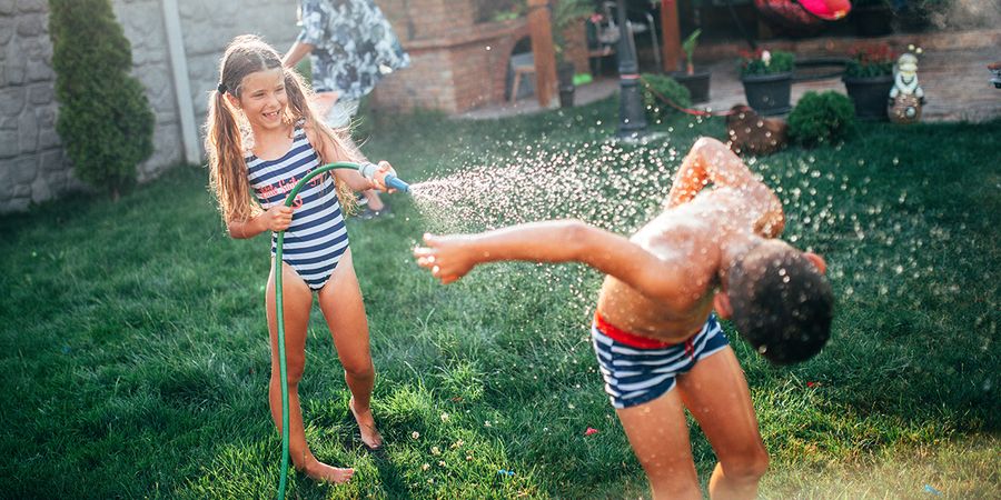 En jente og en gutt leker i hagen med en hageslange, et gøyalt staycation-øyeblikk fra fotoknudsen sin guide til å planlegge den perfekte staycationen.