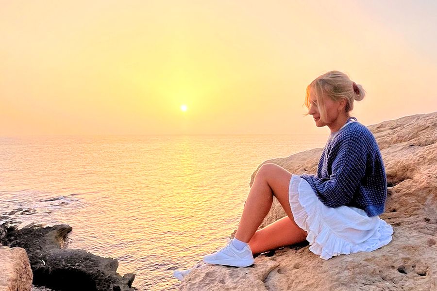 En kvinne sitter på steiner og ser ut over havet og solnedgangen, som fanger stemningen i fotoknudsen sine eventyrlige staycation-ideer.
