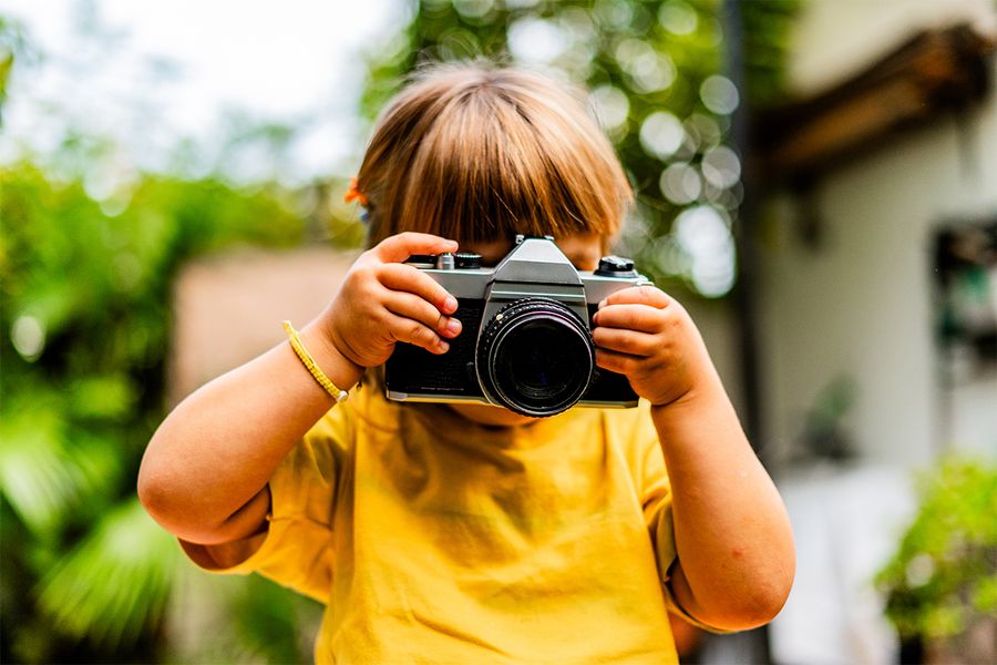 En ung jente tar bilder med et kamera, som gjenspeiler fotoknudsen sine kreative staycation-ideer.