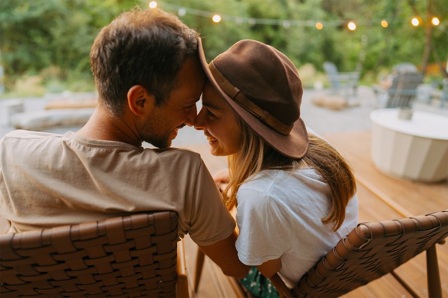 En mann og en kvinne sitter tett inntil hverandre i en hage pyntet med lyslenker, et romantisk øyeblikk fra fotoknudsen sine staycation-ideer for par.