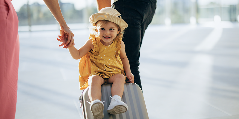 En liten jente sitter på en koffert som blir dratt av gårde, og bildet fanger et lekent øyeblikk fra sommerferie med barn og familieferie med fotoknudsen.
