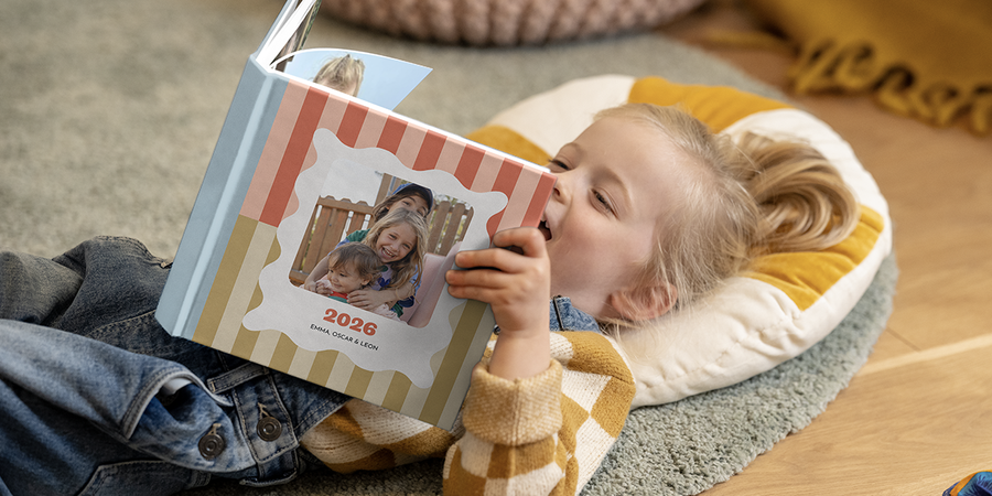 Et barn blar i og smiler til en personlig familiefotobok fra fotoknudsen, en hyggelig aktivitet på reise og en fin måte å bevare minner fra familieferien.
