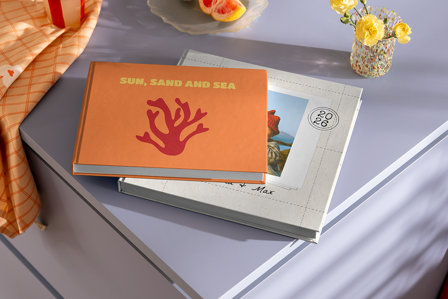 To fotobøker ligger stablet på hverandre, der den øverste boken har et korallmotiv og titelen 'Sun, Sand and Sea', som illustrerer fotoknudsen sine fotobok tittel ideer for strandferie.