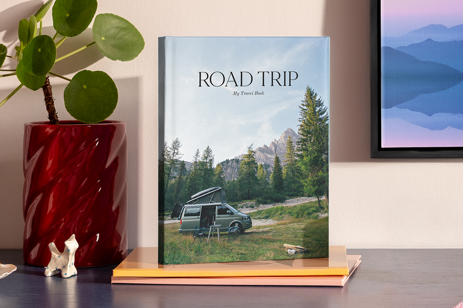 En stor stående fotobok viser et bilde av en bobil i et fjellandskap som ligner en nasjonalpark, som illustrerer fotoknudsen sine fotobok tittel ideer for bilferie.