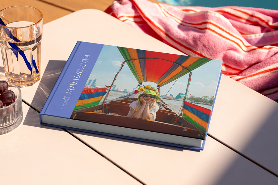 En stor liggende reisefotobok med titelen 'Nomadic Anna' ligger på et bord, med et bilde av en jente på reise på forsiden, som illustrerer fotoknudsen sine fotobok tittel ideer for reise.