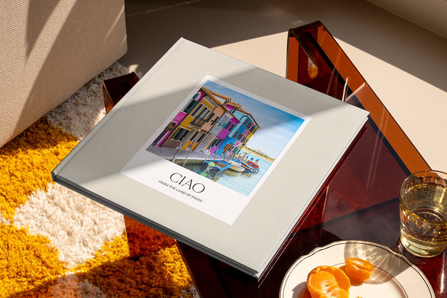 En fotobok med en kanal og fargerike hus i Italia på forsiden heter 'Ciao from the Land of Pasta', som illustrerer fotoknudsen sine fotobok tittel ideer for byreiser.