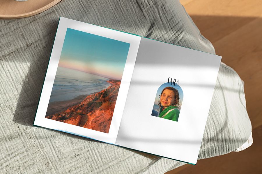 En åpen fotobok viser et vakkert landskap på én side og et bilde av en jente med bildeteksten 'Sara' på den andre, som illustrerer fotoknudsen sitt Artisan Masking-design med lekne rammer inspirert av vintage postkort og frimerker.