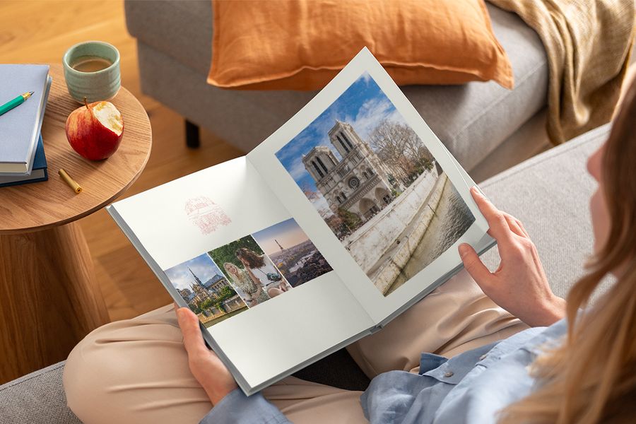 En kvinne holder en åpen fotobok i skjørtet med forskjellige reisebilder, som illustrerer fotoknudsen sitt Graphic Getaways-design inspirert av vintage reiseplakater og illustrerte bykart.
