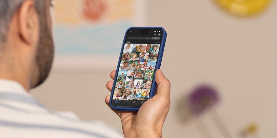 En mann holder telefonen sin og blar gjennom kamerullen, som illustrerer fotoknudsen sin guide til å håndtere bildeoverbelastning og rydde i bildene.