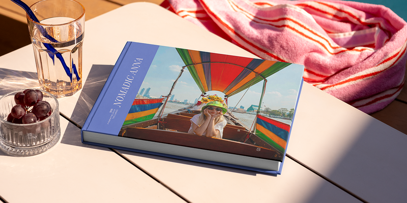 En stor liggende reisefotobok med titelen 'Nomadic Anna' ligger på et bord, med et bilde av en jente på reise på forsiden, som illustrerer fotoknudsen sine fotobok tittel ideer for reise.