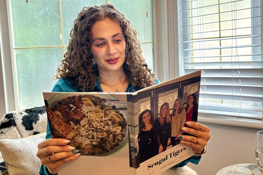 Sarah, som jobber hos fotoknudsen, sitter i en kustol med kumønster og ser på sin personlige familiekokebok, der forsiden viser fire kvinner, inkludert Sarah selv, som illustrerer hvordan en fotobok med oppskrifter samler familieoppskrifter og minner.