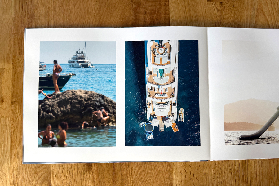 Et åpent oppslag fra Charl van Rooys fotobok viser feriescener på stranden, med folk som slapper av ved havet og en yacht, som illustrerer den visuelle flyten i fotografiporteføljen hans.