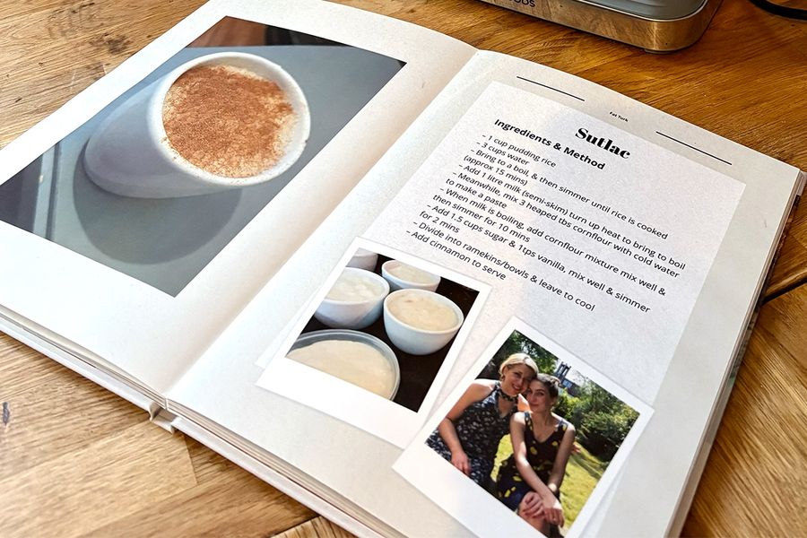 Sarahs åpne oppskriftsbok ligger på kjøkkenbenken og viser sitt layflat-fotobokformat, med bilder av tyrkisk rispudding på venstre side og familiens tilhørende oppskrift på høyre side, som illustrerer fotoknudsen sitt tips om å velge et layflat-design som er lett å lage mat fra.