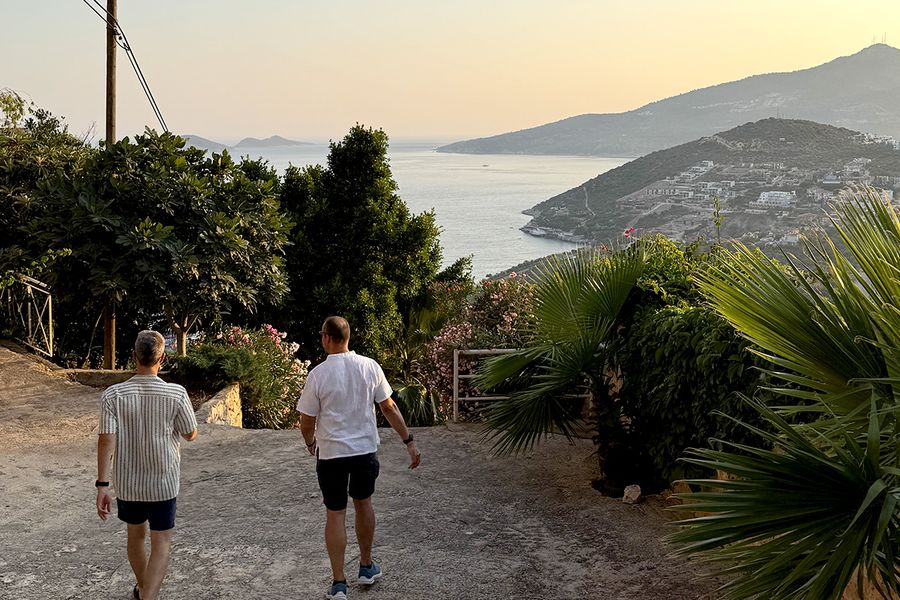 To menn går ned en høyde omgitt av planter mot havet i Kalkan, som fanger sjarmen ved en tyrkisk septemberferie ved Turkis-kysten.