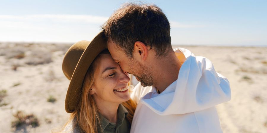Et par i trettiårene smiler og omfavner hverandre i en strandaktig, ørkenlignende omgivelse, som introduserer fotoknudsen sin guide med 60 idéer til meldinger i et bryllupsdagskort.
