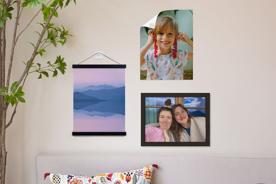 Ulike alternativer for å henge opp veggkunst fra fotoknudsen vises i et hjem, inkludert en personlig plakat av en ung gutt festet med limstrimler, en personlig landskapsplakat hengt opp med en trehenger og limkrok, og et innrammet bilde av to smilende jenter.