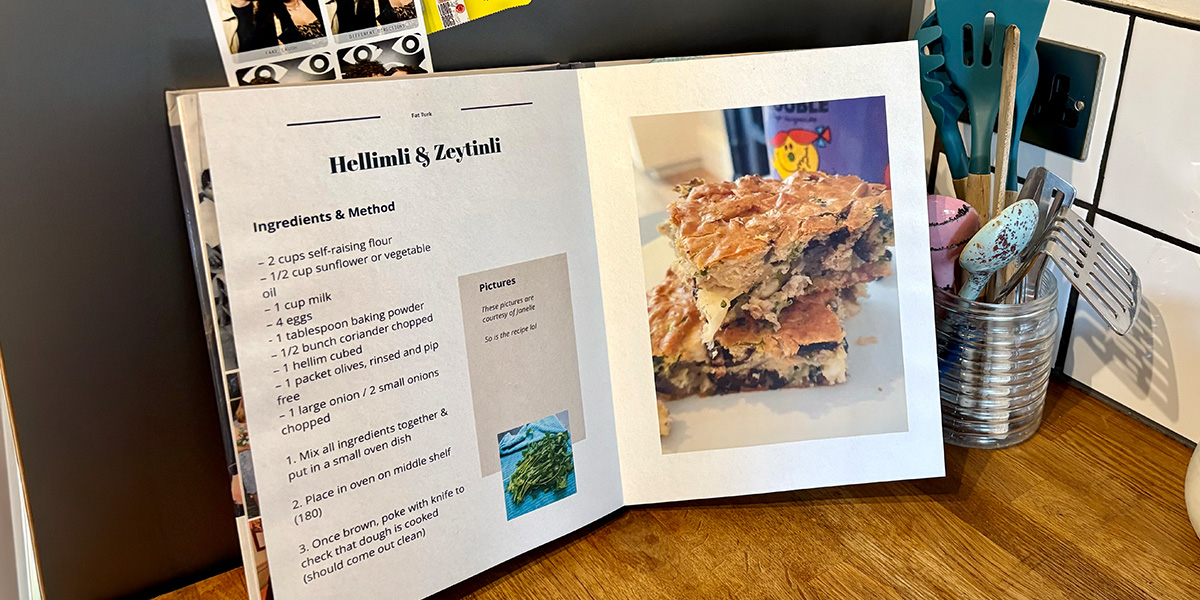 En åpen personlig kokebok ligger på et kjøkken, med en krukke med skjeer og kjøkkenredskaper i bakgrunnen, som introduserer fotoknudsen sin guide til å lage din egen kokebok.