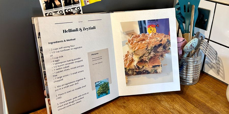 En åpen personlig kokebok ligger på et kjøkken, med en krukke med skjeer og kjøkkenredskaper i bakgrunnen, som introduserer fotoknudsen sin guide til å lage din egen kokebok.