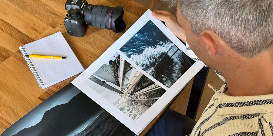 Fotograf Charl van Rooy ser ned på porteføljen sin, med kameraet og en notatbok på bordet ved siden av seg, som introduserer fotoknudsen sin guide til å lage en fotografiportefølje som fotobok.