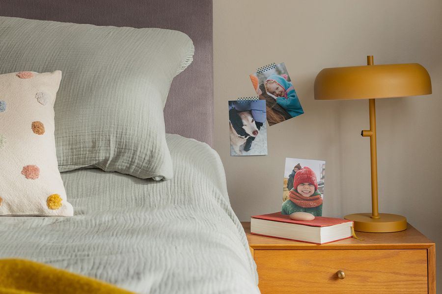 Et utvalg familiefotoutskrifter henger på veggen ved siden av en seng, som illustrerer hvordan fotoknudsen sine fotoutskrifter gir en lun og personlig touch til et hygge-soverom.
