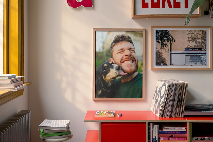 En rød skjenk med en platespiller og plater, med bøker under og ved siden av, og personlig veggkunst over, blant annet en innrammet plakat av en mann og hunden hans, som illustrerer hvordan fotoknudsen sin veggkunst fornyer stuens vegger for en lun høststemning.