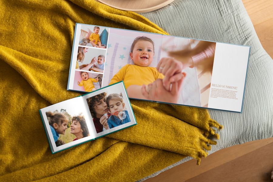 To personlige fotobøker ligger åpne med familiebilder, hvilende på et sennepsgult pledd, som illustrerer hvordan fotoknudsen sine fotobøker passer inn i et hygge-hjem.