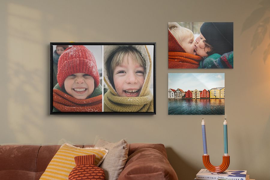 Tre eksempler på personlig veggkunst henger over en sofa i en stue, høstlige familiebilder med smilende barn i vinterklær, som illustrerer hvordan fotoknudsen sin veggkunst gir en lun hygge-stil til hjemmet.
