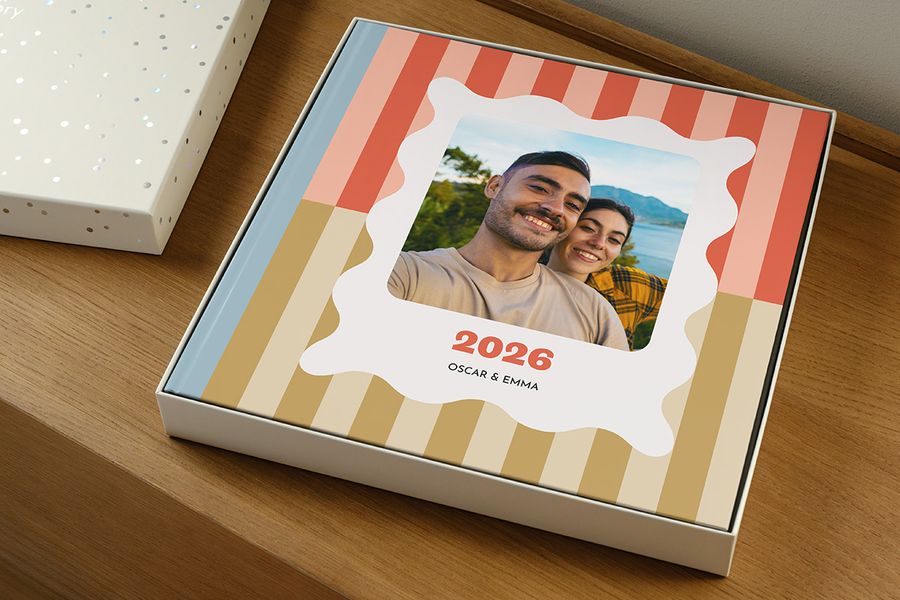 En fotobok ligger i gaveboksen uten lokket, og ser ut som en årbok merket '2026' med et smilende par på forsiden, som illustrerer hvordan man velger riktig størrelse presentasjonsboks til fotoboken sin.