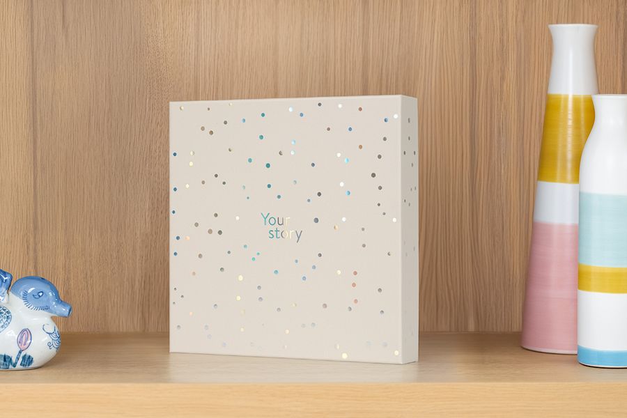 Presentasjonsboksen står på en hylle ved siden av en vase og dekorasjoner, som illustrerer hvordan den også fungerer som en attraktiv oppbevaringsboks for fotoalbum.