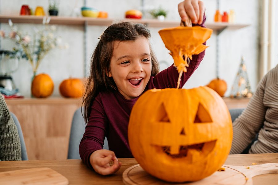 Et barn løfter toppen av et gresskar det nettopp har skåret ut, som illustrerer fotoknudsen sine morsomme og søte gresskaruttrykk for Halloween-bildetekster på Instagram.