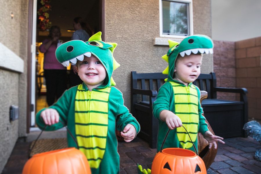 To små gutter i dinosaurkostymer går på knask eller knep med gresskarkurver i hendene, som illustrerer fotoknudsen sine Halloween-uttrykk for bilder fra knask eller knep.