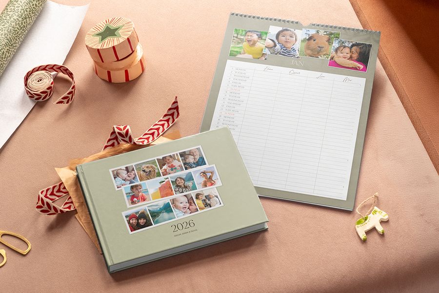 En salvegrønn fotobok med 2026 på forsiden og en veggkalender for familien med bilder øverst og kolonner for hvert familiemedlem, til illustrasjon av fotoknudsen sine delbare familiekalendere til Black Friday-julegaver.